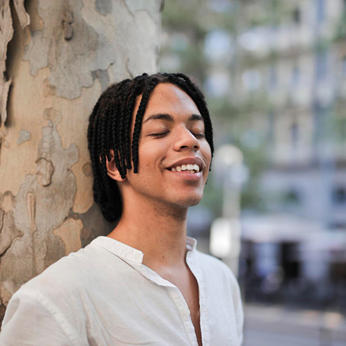 Latino man leaning against a tree looking calm and relaxed.